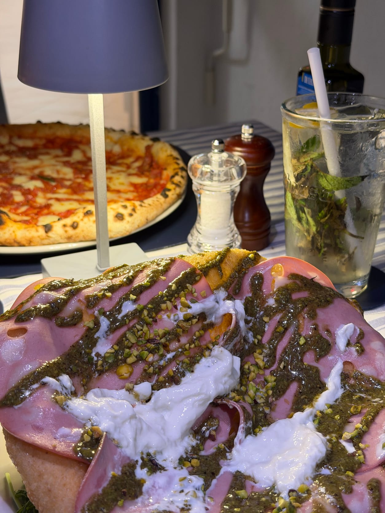 Pizza fritta con mortadella, pesto di pistacchio e stracciatella, con una pizza e una lampada sullo sfondo
