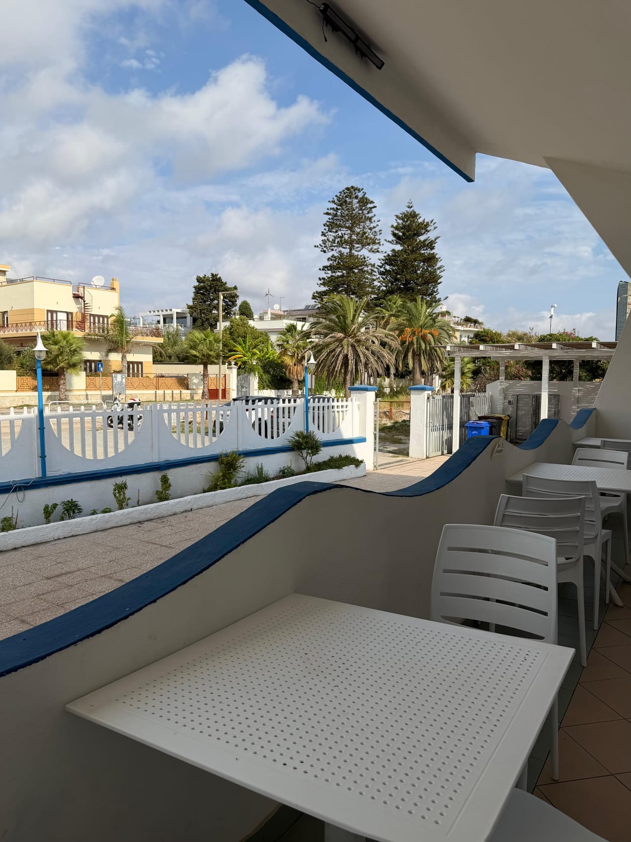 Vista dalla terrazza verso il Viale Poetto: cancellata bianca, lampioni blu e palme