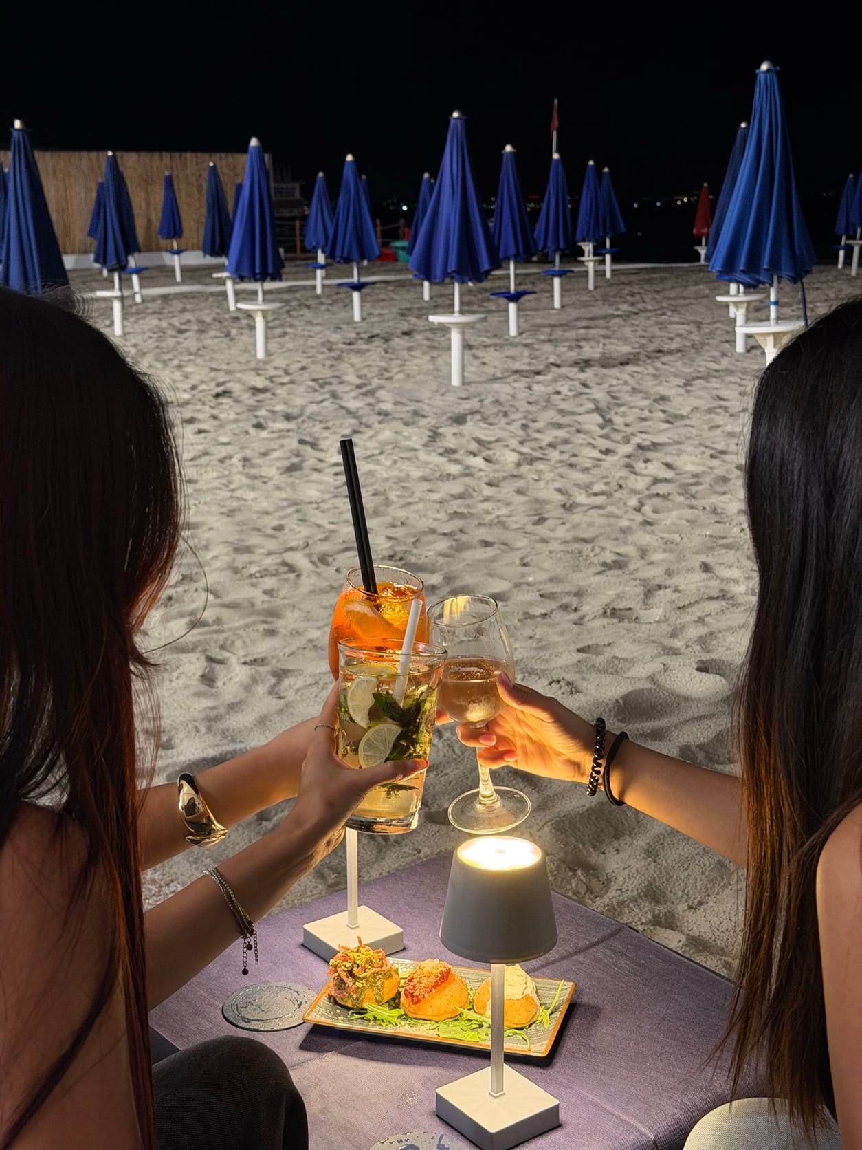 Due amiche brindano sulla spiaggia del Poetto di sera