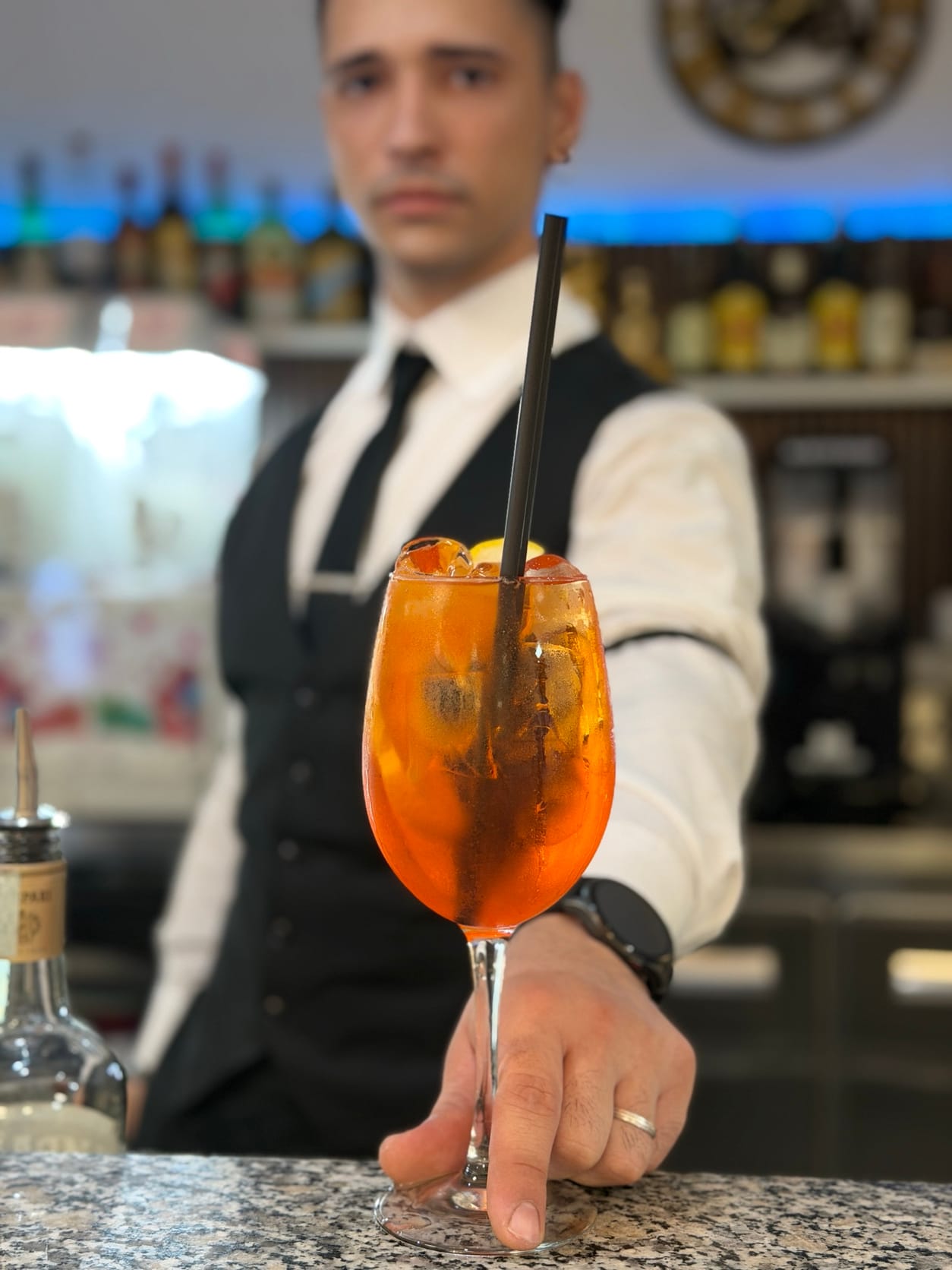 Un barman in gilet e cravatta porge uno spritz al bancone
